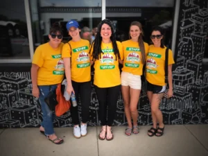Five staff members wearing yellow Lumberday event shirts pose together outside a building.